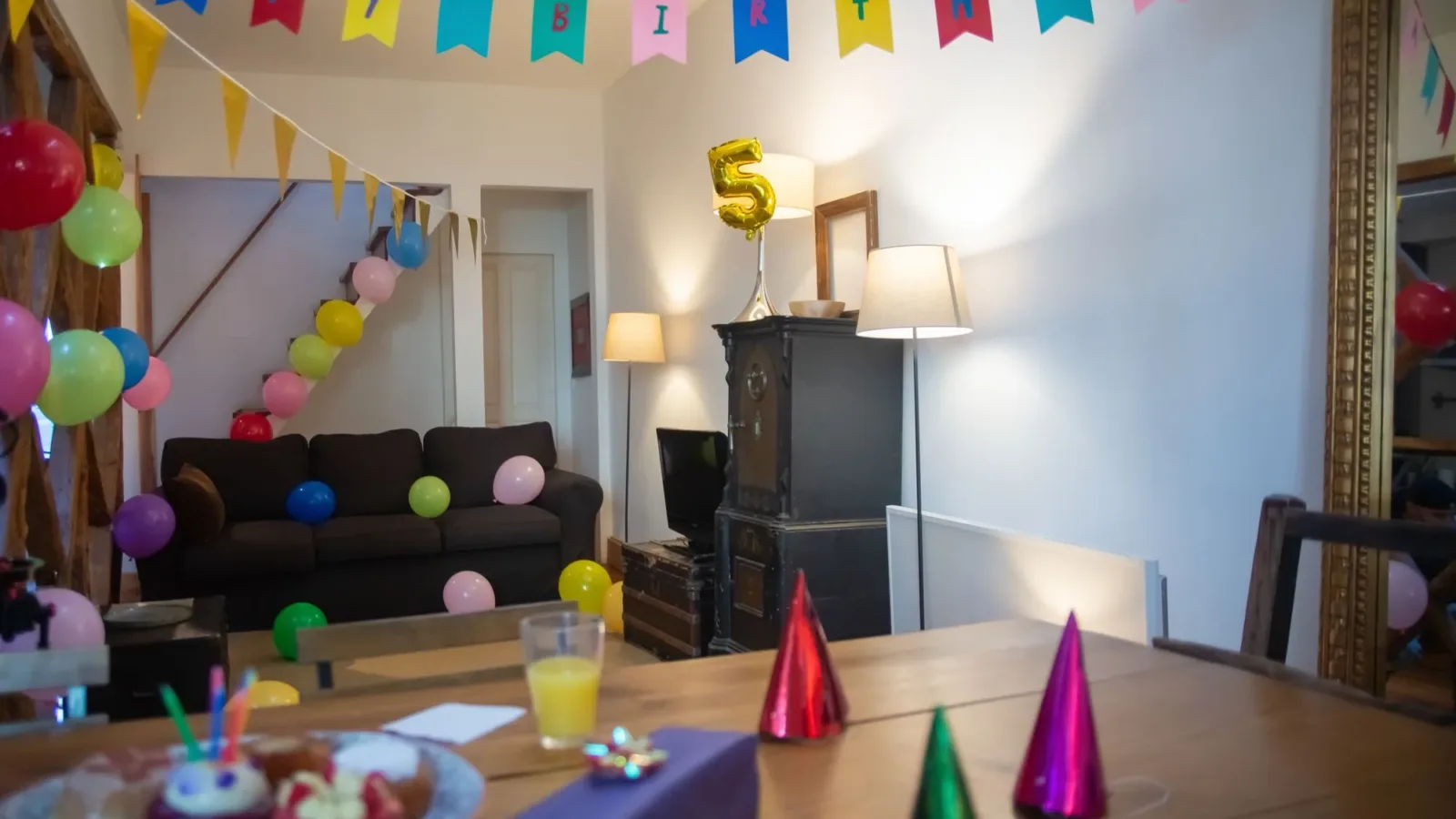 Indoor 5th birthday party setup with balloons, banners, and party hats in a cozy home setting.