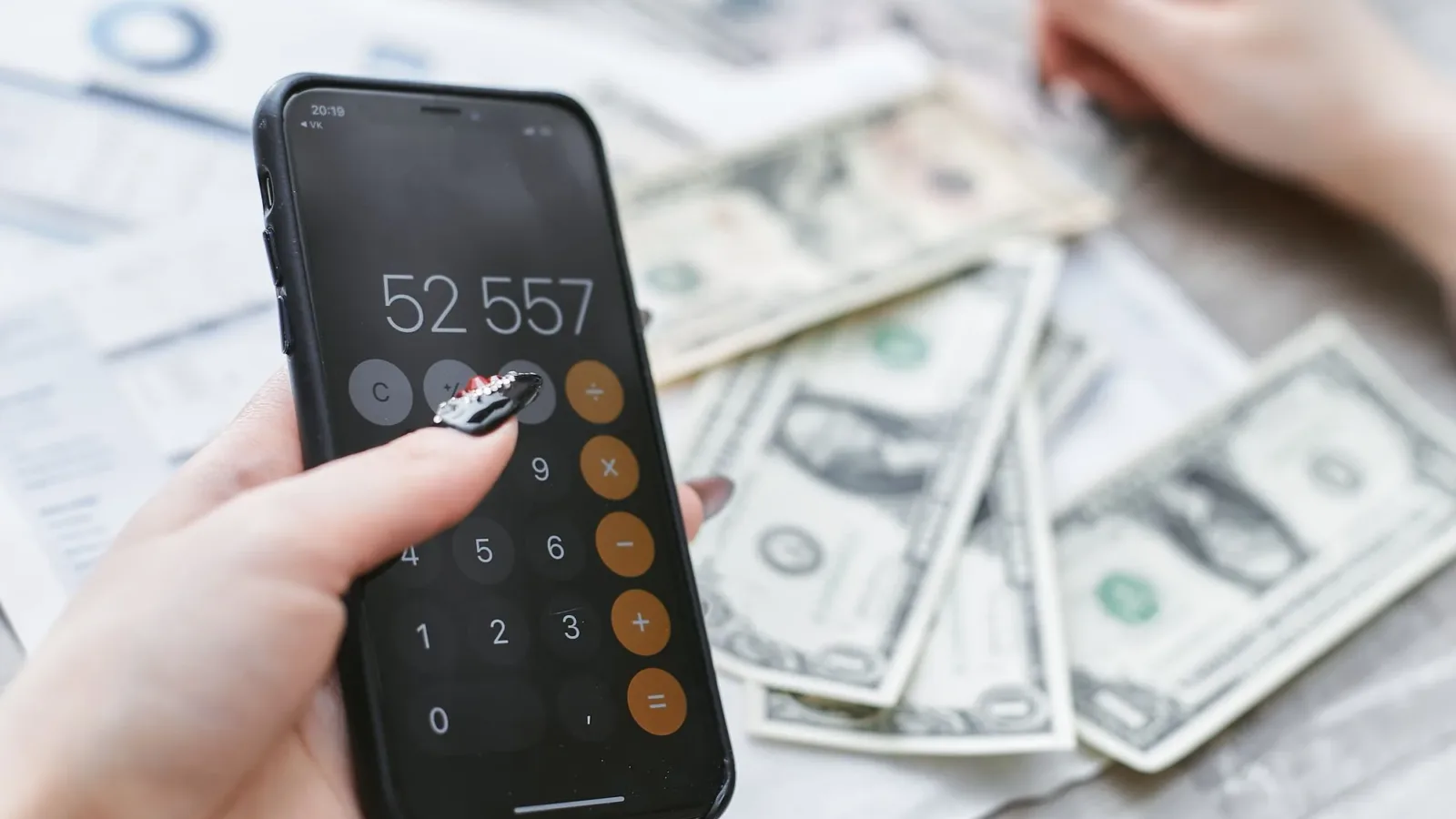 Close-up of hands using smartphone calculator next to dollar bills on table. Financial planning concept.