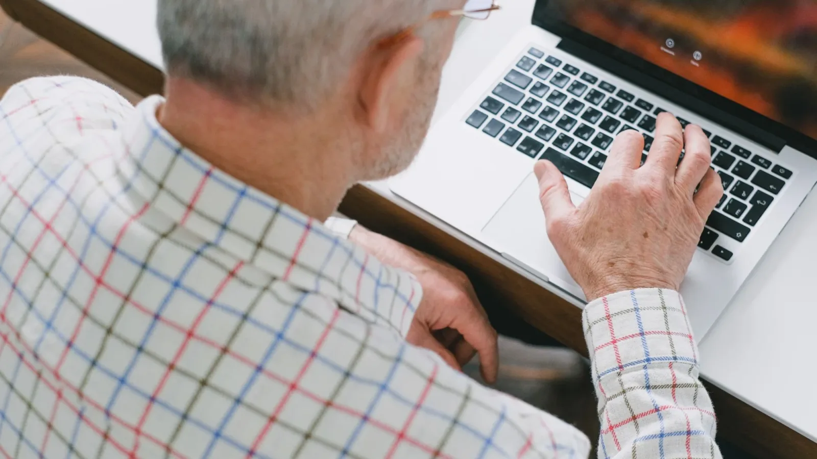 A senior adult in a plaid shirt using a laptop, showcasing digital engagement.