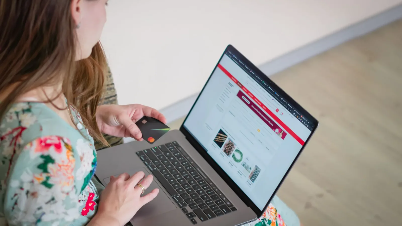 Woman in floral dress shopping online with a laptop and credit card indoors.