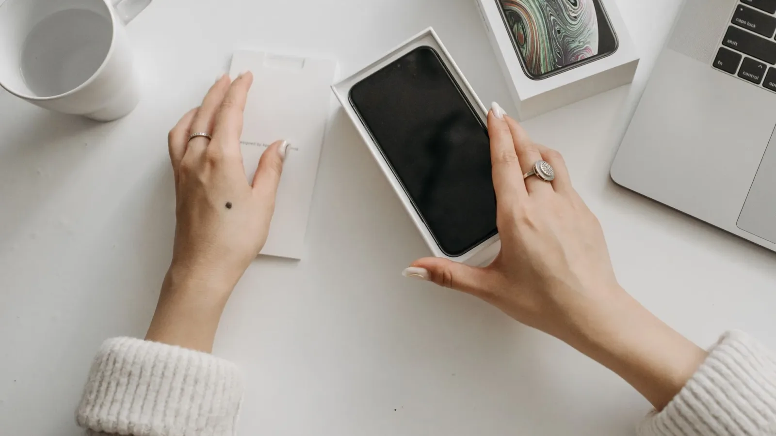 Woman unboxing a smartphone on a white table, showcasing technology and lifestyle