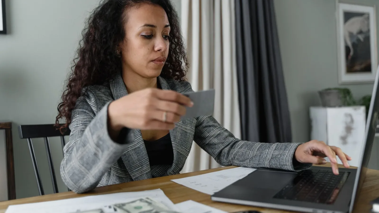 Woman using a laptop and managing finances with cash and card on a wooden table indoors.
