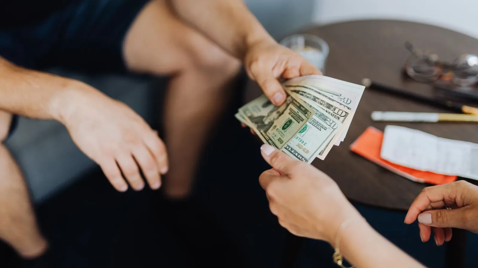Close-up of hands exchanging US dollar bills, symbolizing a financial transaction or payment.
