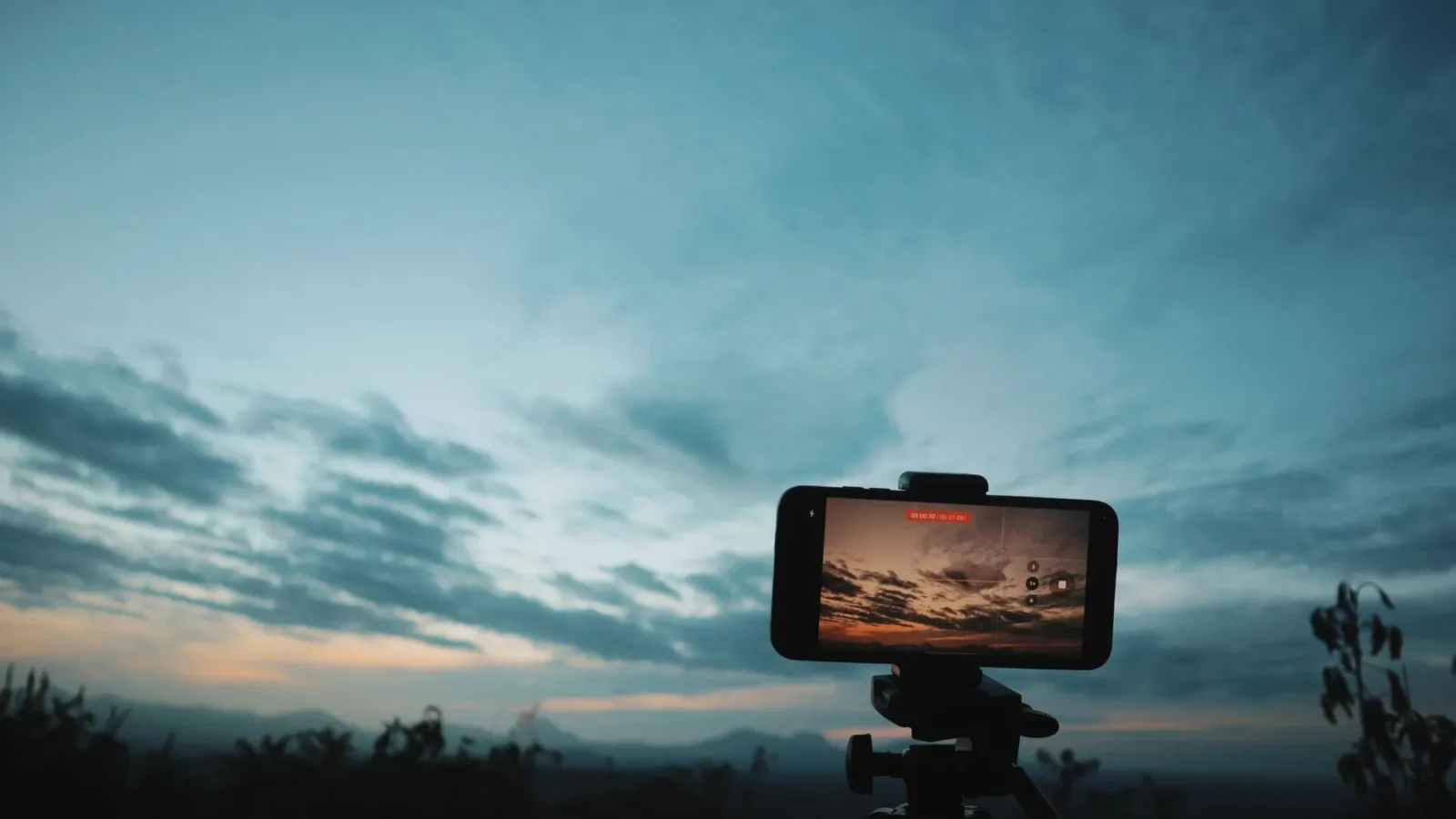 Smartphone on tripod photographing stunning sunset landscape view.