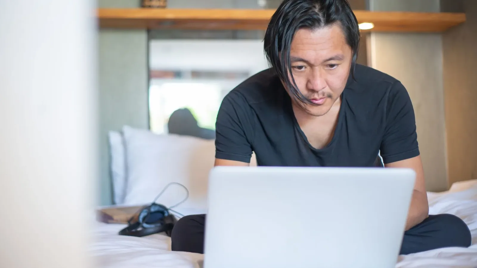 An Asian man working from home on a laptop, focusing on his digital tasks in a cozy indoor setting.
