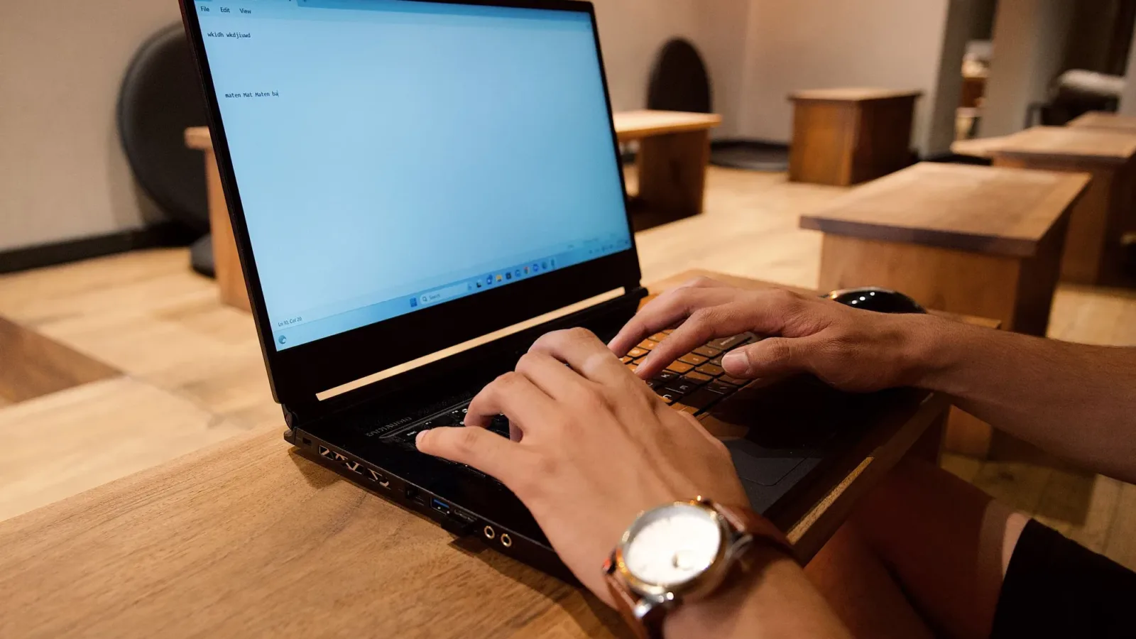 A person working on a laptop in a modern office setting, focused on typing.